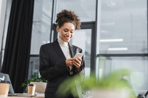 Cheerful african american businesswoman using mobile phone in office — Stock Photo