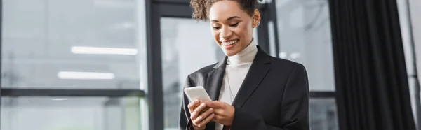 Femme d'affaires afro-américaine positive utilisant un téléphone portable au bureau, bannière — Photo de stock