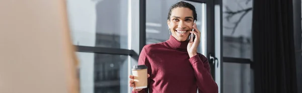 Un uomo d'affari afro-americano positivo che parla al cellulare e tiene il drink da asporto in ufficio, striscione — Foto stock