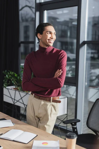 Lächelnder afrikanisch-amerikanischer Geschäftsmann steht neben Coffee to go und Notizbuch im Büro — Stockfoto