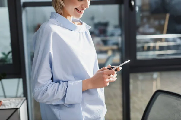 Vista cortada de empresária sorridente usando telefone celular no escritório — Fotografia de Stock