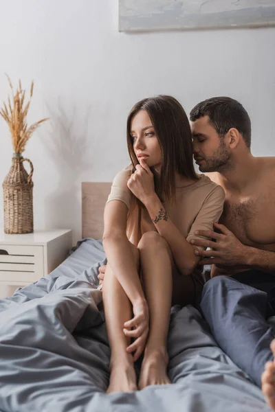 Sexy homem beijos pensivo namorada no t-shirt no cama no casa — Fotografia de Stock