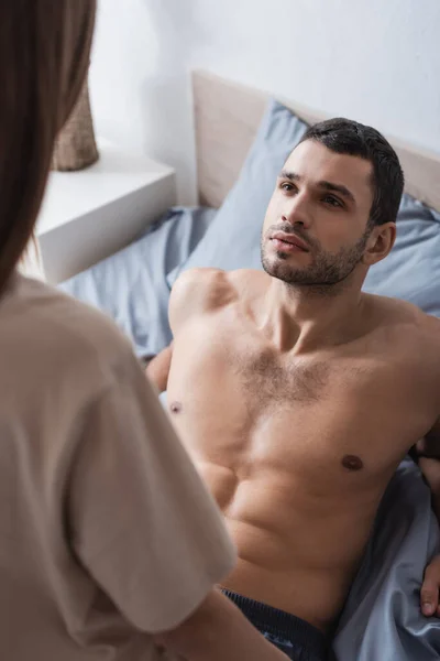 Sexy muscular man looking at blurred girlfriend on bed — Stock Photo