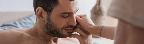 Femme tatouée touchant petit ami torse nu avec les yeux fermés sur le lit, bannière — Photo de stock