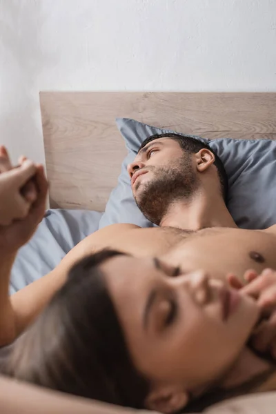 Shirtless man holding hands of blurred girlfriend on bed at home — Stock Photo