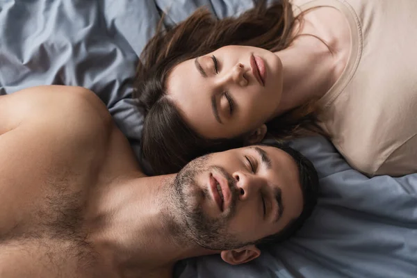 Top view of brunette woman lying near shirtless boyfriend on bed — Stock Photo