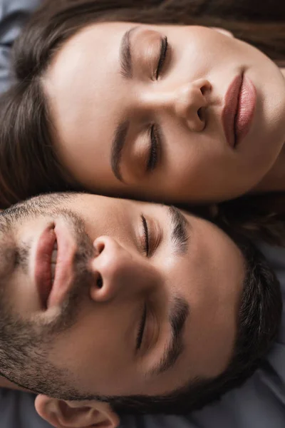 Вид сверху молодой пары с закрытыми глазами, лежащей на кровати — стоковое фото