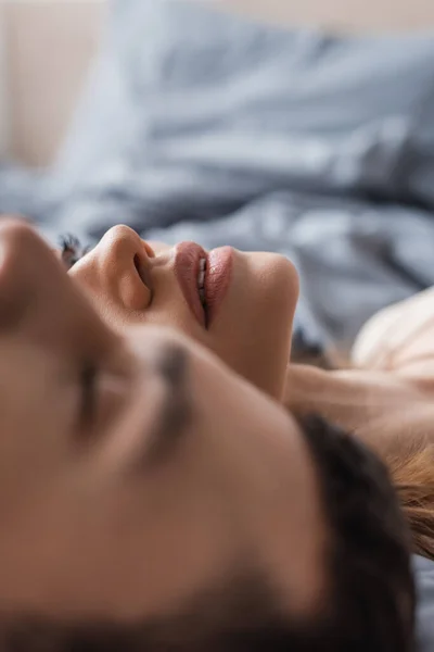 Mujer joven tendida cerca borrosa novio en la cama en casa — Stock Photo