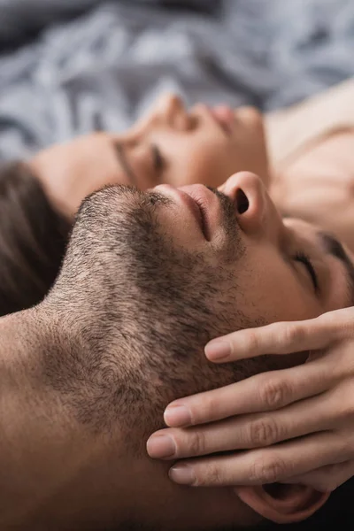 Mujer borrosa tocando la mejilla del novio en la cama en casa - foto de stock