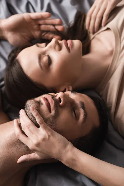 Vista de ángulo alto de la mujer bonita tocando el cuello del novio en la cama - foto de stock