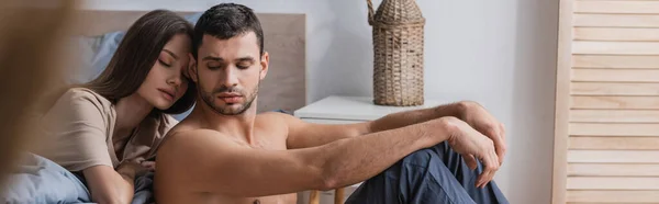 Muscular man sitting near girlfriend with closed eyes in bedroom, banner — Stock Photo