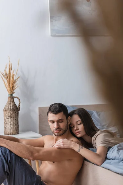 Brünette Frau mit geschlossenen Augen berührt muskulösen Mann im Schlafzimmer — Stockfoto