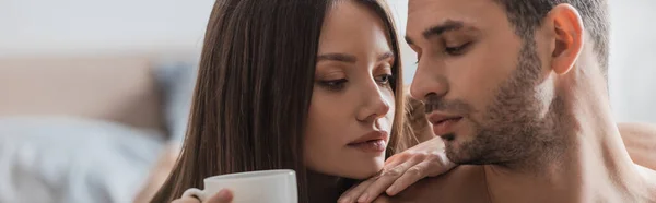 Mujer bonita sosteniendo café cerca de hombre de mierda en el dormitorio, pancarta - foto de stock