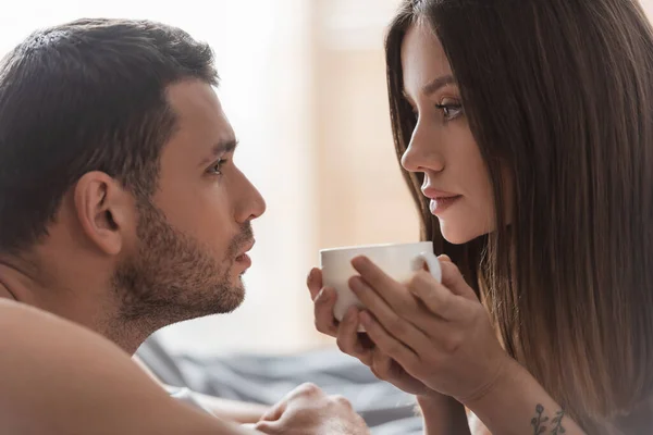 Jovem segurando xícara de café e olhando para o namorado no quarto — Fotografia de Stock