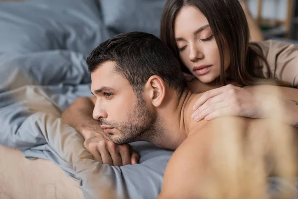 Bruna donna con gli occhi chiusi toccare uomo muscolare sul letto sfocato — Foto stock