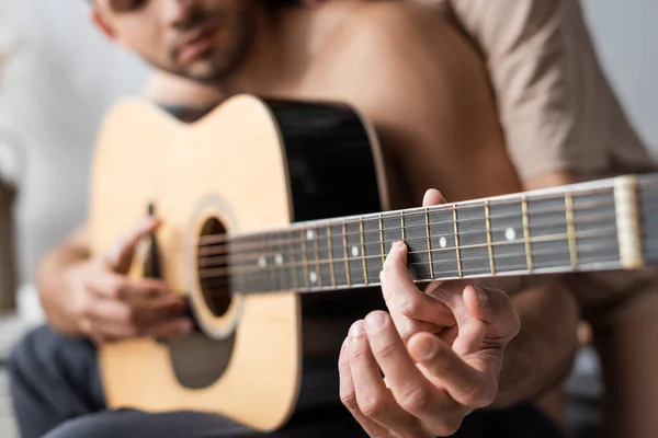 Vista recortada de pareja borrosa tocando la guitarra acústica en casa - foto de stock