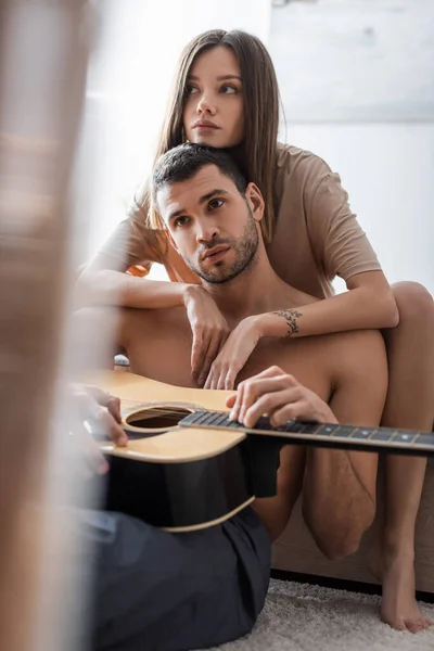 Mujer morena abrazando novio sexy con guitarra acústica en casa - foto de stock