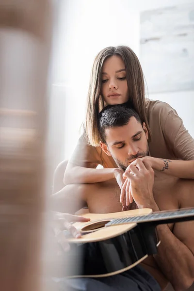 Hemdloser Mann hält Akustikgitarre und küsst Freundin zu Hause — Stockfoto