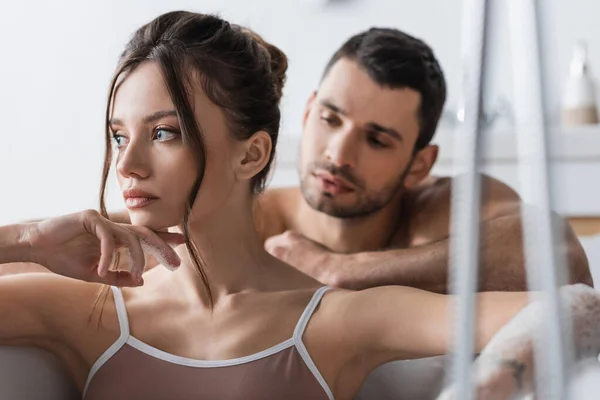 Brunette woman taking bath near blurred shirtless boyfriend at home — Stock Photo