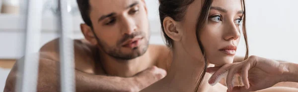 Mujer morena mirando lejos cerca de novio sin camisa en el baño, pancarta - foto de stock