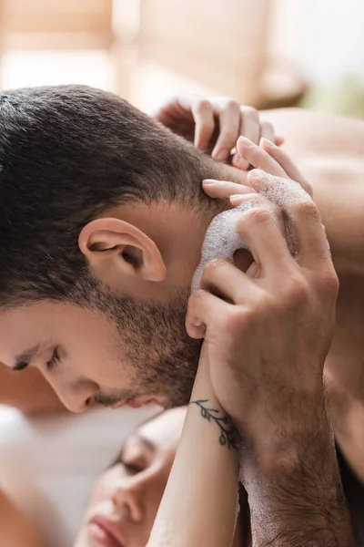 Homme barbu touchant les mains d'une petite amie floue prenant un bain à la maison — Photo de stock