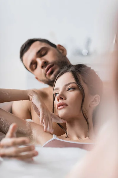 Jeune femme prenant un bain avec de la mousse et petit ami flou à la maison — Photo de stock