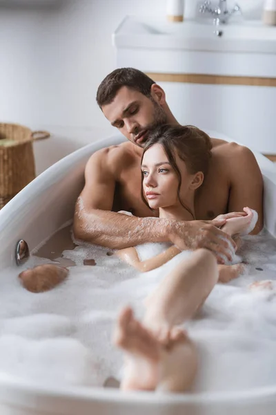 Homem muscular abraçando namorada na banheira com espuma em casa — Fotografia de Stock