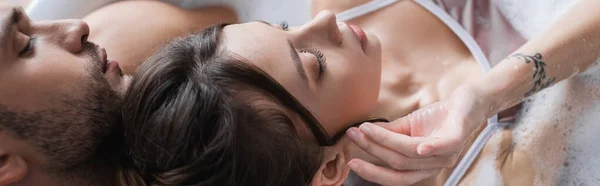 Overhead view of young woman touching hair while taking bath with boyfriend at home, banner — Stock Photo