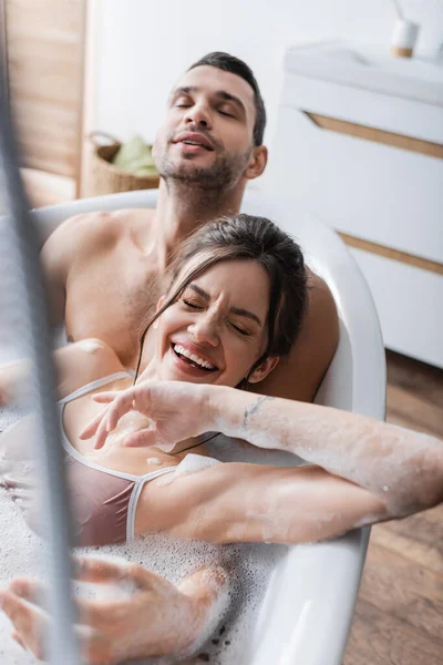 Mujer joven riendo mientras toma un baño con su novio en casa - foto de stock