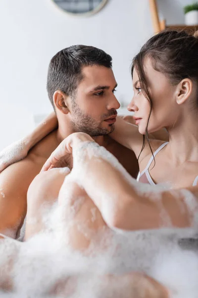 Молода пара дивиться один на одного, приймаючи ванну з піною вдома — стокове фото