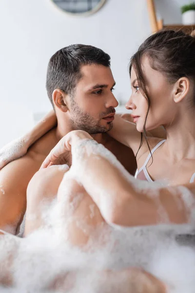 Pareja joven mirándose mientras se bañan con espuma en casa - foto de stock