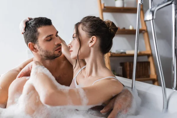 Молода жінка обіймає і дивиться на хлопця в ванній з піною — стокове фото