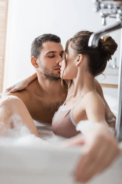 Homem muscular beijando morena namorada no banho com espuma em casa — Fotografia de Stock