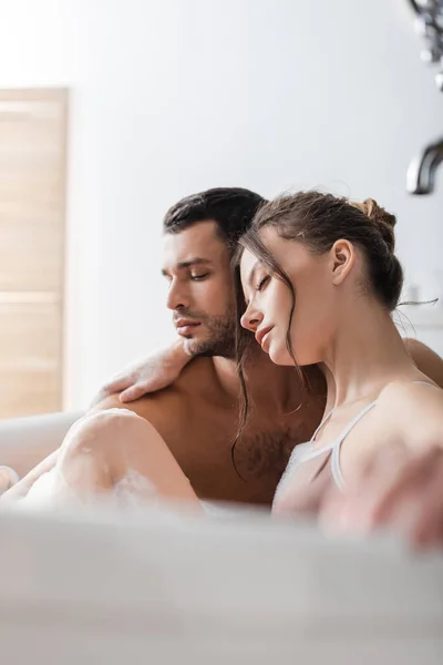 Mujer morena abrazando novio en baño con espuma en casa - foto de stock