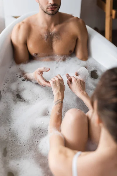 Jeune couple tenant la main tout en prenant un bain avec de la mousse à la maison — Photo de stock