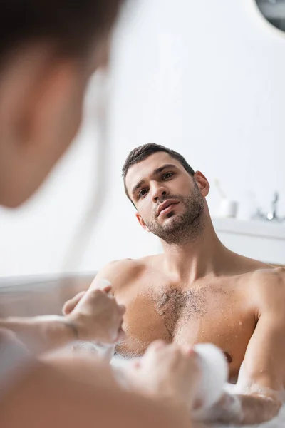 Muskulöser Mann hält Hände von verschwommener Freundin in Badewanne — Stockfoto