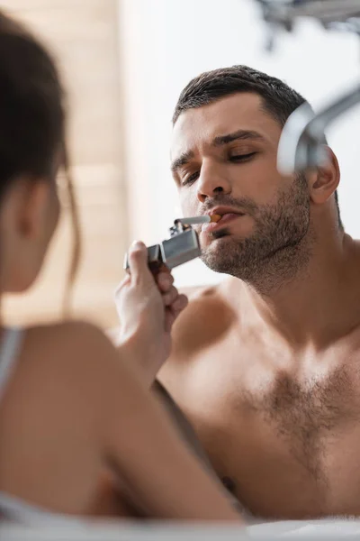 Mulher desfocada segurando isqueiro perto de homem sem camisa com cigarro na banheira — Fotografia de Stock