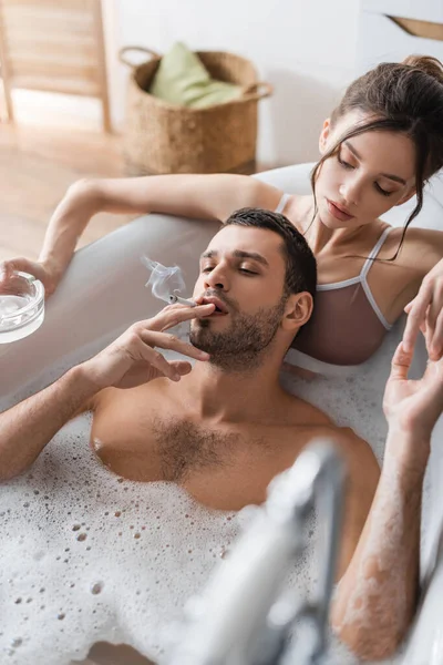Barbudo hombre fumar cigarrillo cerca de novia con cenicero en bañera - foto de stock