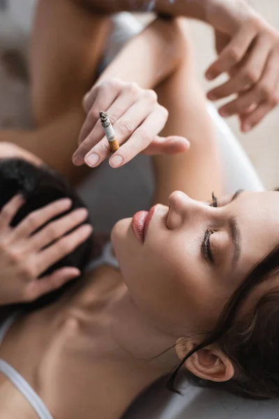 Vue du dessus d'une jolie jeune femme tenant une cigarette près d'un homme flou dans une baignoire — Photo de stock