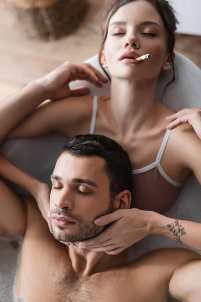 Vista dall'alto della donna bruna con gli occhi chiusi che fuma e tocca il fidanzato barbuto in bagno — Foto stock