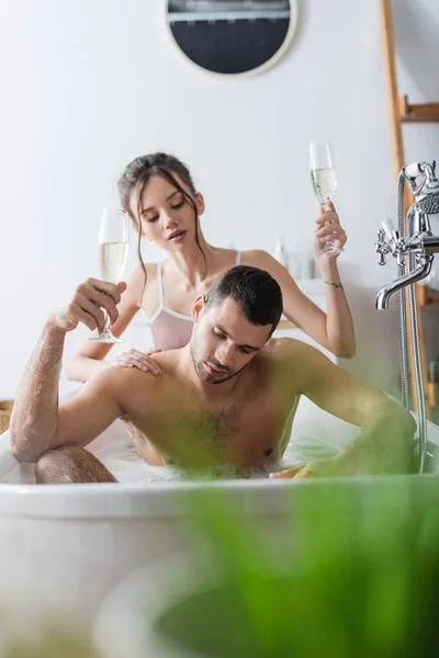 Woman holding glass of champagne near muscular boyfriend in bathtub — Stock Photo