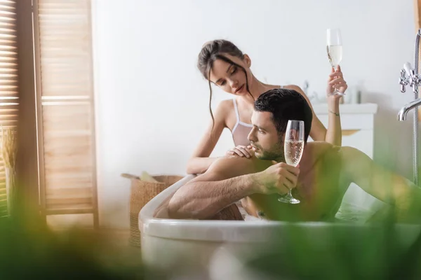 Mujer tocando novio muscular con champán en la bañera - foto de stock