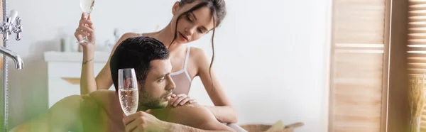Pretty woman touching muscular man with glass of champagne in bathtub, banner — Stock Photo
