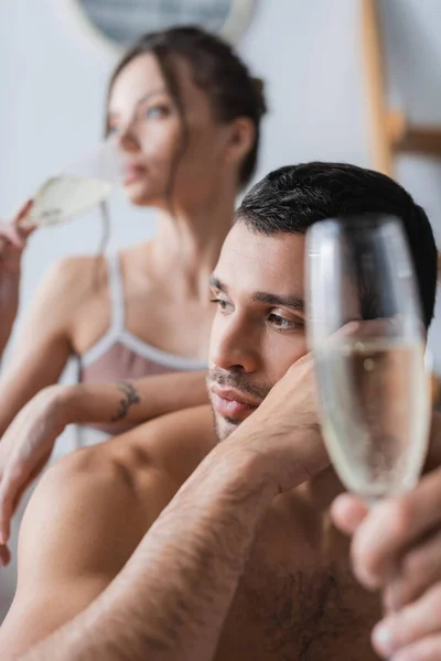 Homem musculoso segurando copo borrado de champanhe perto da namorada em casa — Fotografia de Stock