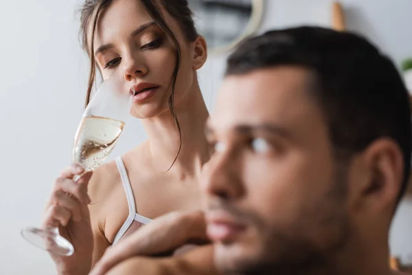 Hübsche Frau hält Glas Champagner neben verschwommenem Freund zu Hause — Stockfoto