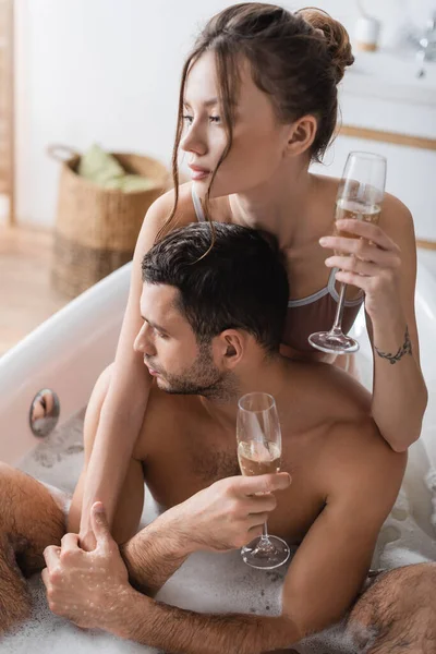 Woman holding glass of champagne and embracing boyfriend with champagne in bathtub — Stock Photo