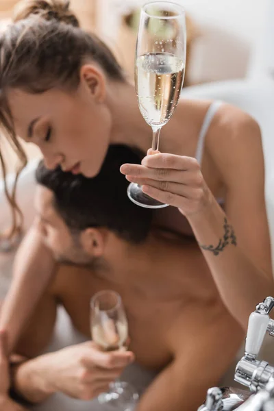 Bicchiere di champagne in mano di donna sfocata vicino a fidanzato in vasca da bagno — Foto stock