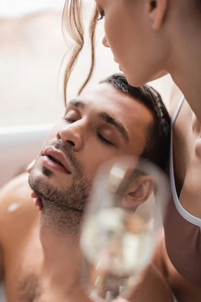 Mujer sosteniendo champán borroso y mirando novio barbudo en la bañera - foto de stock