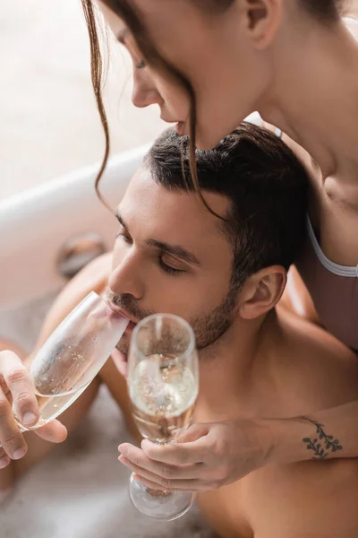 Vista ad alto angolo dell'uomo muscoloso che beve champagne vicino alla ragazza nella vasca da bagno offuscata — Foto stock