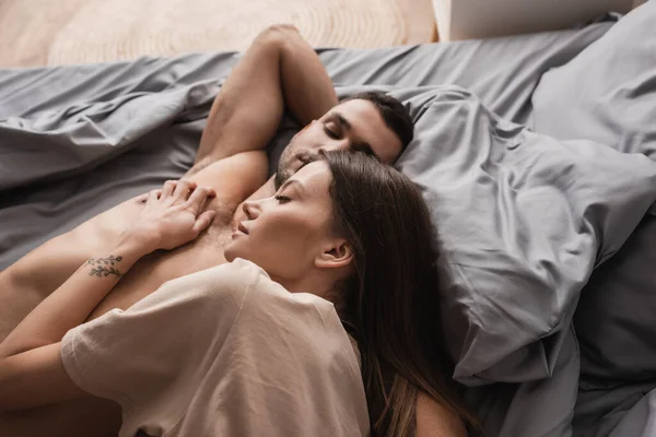 Vista dall'alto della donna in t-shirt sdraiata vicino al fidanzato muscolare sul letto — Foto stock